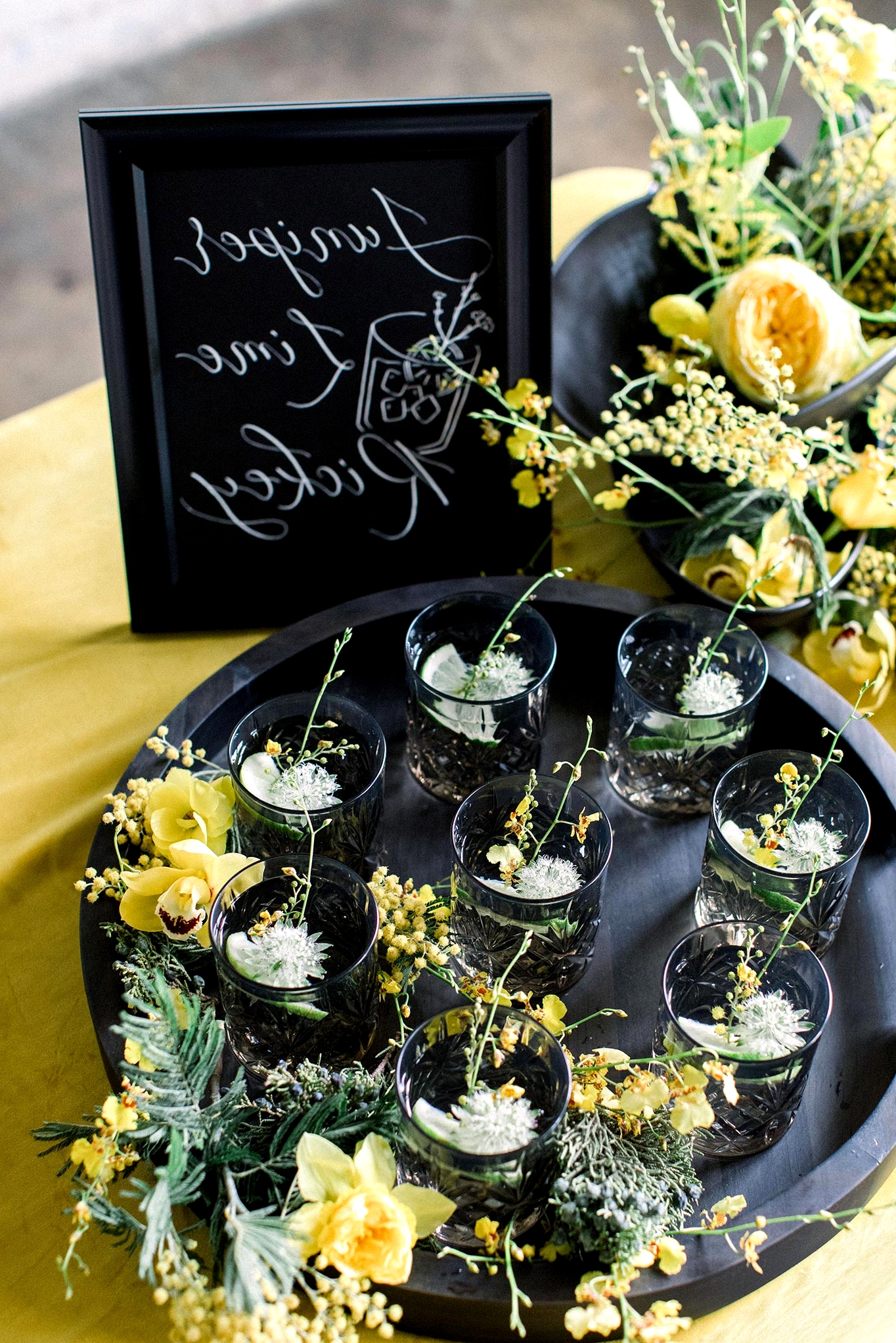 black crystal cut glassware with botanical cocktails on a matte black serving tray with yellow flower accents