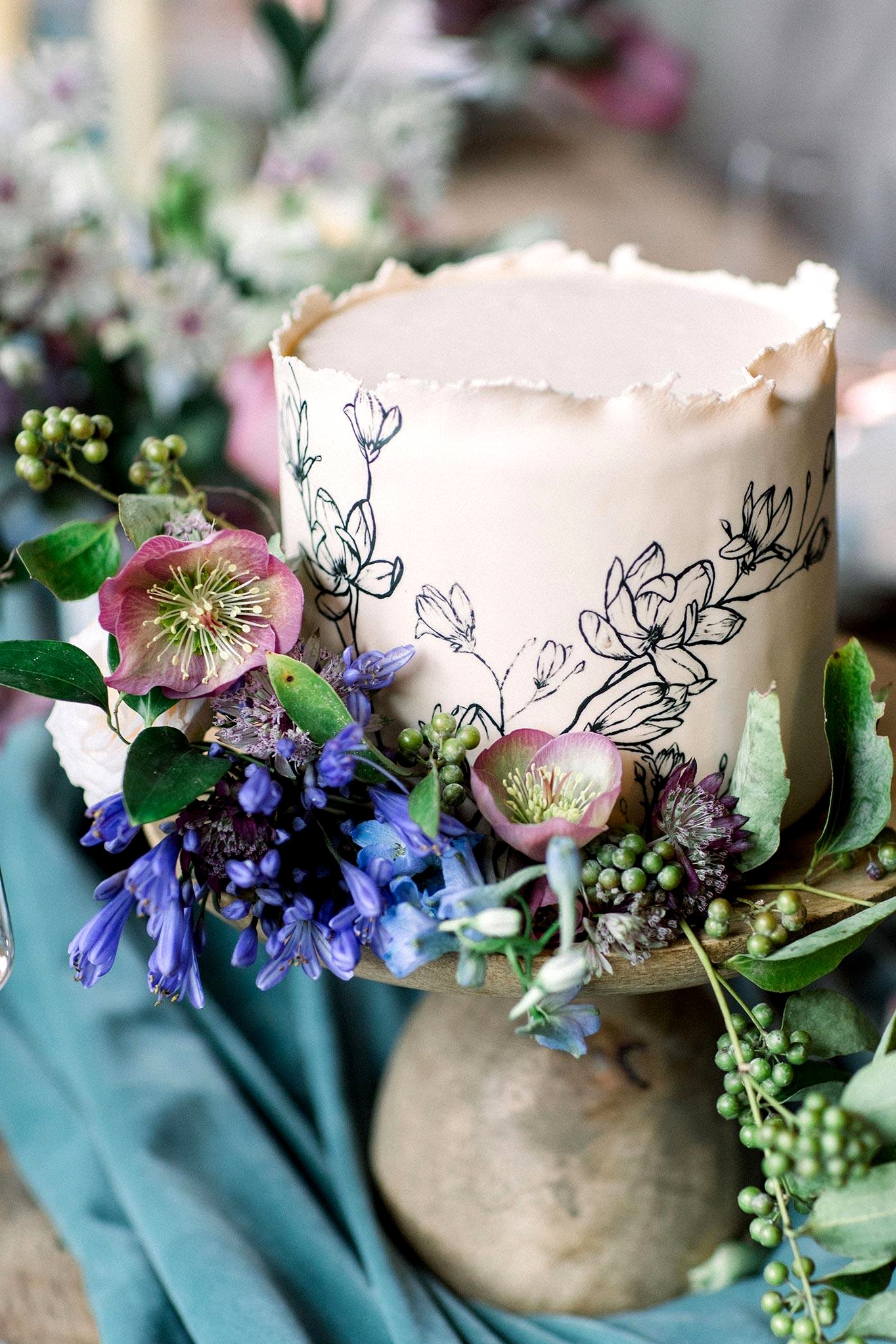 botanical sketch wedding cake with fresh flower accents and a wooden cake stand